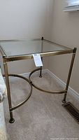 Full view of the square beveled glass top end table with brass colored metal frame and circular base supports.