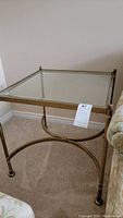 Front left angled view of vintage square end table with brass coloured metal frame and clear beveled glass top, showing its design and condition.