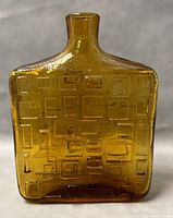 Front view of the amber Empoli glass bottle showing the geometric rectangular embossed design and overall bottle shape.