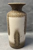 Front view showing the tall cylindrical vase with textured brown glaze and white rectangular accents.
