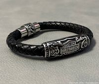 Close-up side view of the braided leather bracelet with detailed view of the metal centerpiece logo showing Harley-Davidson branding and decorative motifs.