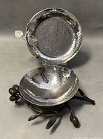 Two artistic hammered metal footed bowls by Michael Aram. One bowl has two decorative leaves on the rim; the other rests on a base shaped like olive branches with olives.