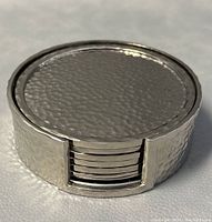 Stacked hammered silver-tone metal coaster set with holder showing textured finish