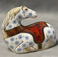 Side angle showing horse's face, blue floral patterns on body, and detailed red saddle with gold trimming.