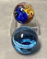 Two art glass paperweights shown, one with multicolor swirl on stand and one with blue swirl without stand