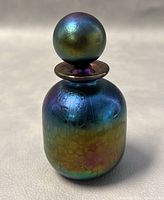 Front view of the signed vintage Phoenician Malta perfume bottle showing iridescent crackled surface and spherical stopper.