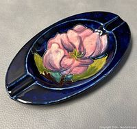 Front angle showing the oval ashtray with a pink hibiscus flower and blue glaze.