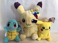 Clear photo of three Pokémon plush toys including Squirtle, unusual Pikachu with floral head accessory, and standard Pikachu, all new with tags.
