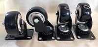 Four black caster wheels arranged in a row, one swivel caster on the left and three fixed casters on the right, showing design and mounting plates.