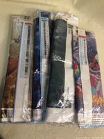 Four rolled diamond painting canvases sealed in plastic, showing charts with symbols and color codes for diamond placement.