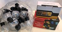Lot showing three sets of LED decorative string lights with globe bulbs and black wiring. One set plugged in, others coiled in packaging and loose.