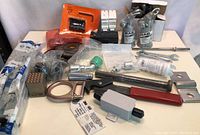 Wide view photo showing multiple new industrial tools, switches, spray bottles, wrenches, and fittings on a white surface.
