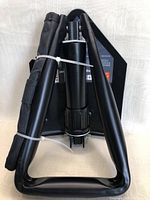 Folded black metal folding camping shovel with triangular handle and attached fabric carrying case secured with zip tie.