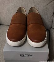 Front view of new brown slip-on men's loafers on Kenneth Cole Reaction box showing ribbed elastic band and white sole.