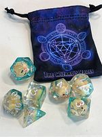 Photo of all seven polyhedral dice with a black drawstring pouch featuring a gem-shaped geometric design and The Wizards Vault label