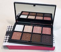Photo of the open eyeshadow palette showing 8 warm nude shades with mirror and packaging underneath.