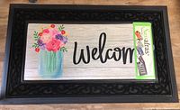 Top view of the black rubber door mat frame with a removable insert showing colorful floral bouquet and 'Welcome' text.