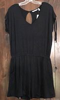 Front view of black romper with short sleeves, elastic waist, and keyhole back detail hanging on a hanger.