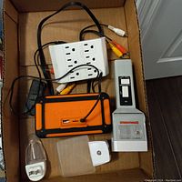 Box containing flashlight, power strip, electrical plugs, night lights, and connectors arranged with cords visible
