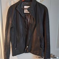Front view of black leather Zara jacket hanging on hanger, showing zipper front and pocket details.