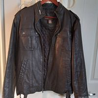 Full front view of black leather jacket hanging on wooden hanger.