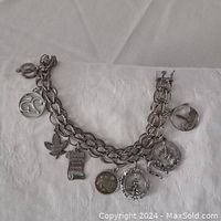 Photo of silver-tone chain bracelet with nine distinct amulets attached, laid flat on white background, showing worn condition and tarnish.