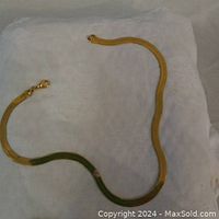 Gold plated chain necklace laid on white cloth background, showing entire length, snake style design, clasp visible.