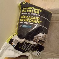 Sealed black bag of EnviroSafe Ice Melter enhanced with CMA, branded with house illustration and bilingual text.