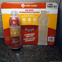 Photo of two-pack First Alert fire spray with one can partially removed from packaging, showing label details.