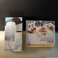 Photo showing boxed Starfrit Deluxe Rotary Grater with grating cone attachments on box image and boxed Westinghouse coffee grinder with coffee beans image on box.