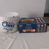 Photo of a stack of Royal Chinet disposable dinner plates and a Kirkland box of crystal clear cutlery on a table