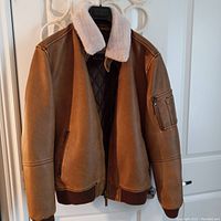 Front view of light brown leather bomber jacket with white fur collar hanging on a hanger