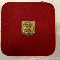 Closed red velvet jewelry box with gold crest emblem on the lid.