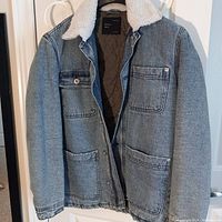 Front view of men's light blue denim jean jacket with white faux fur collar, four pockets visible, unbuttoned and open to show quilted inner lining