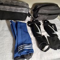 Photo showing all items: men's blue soccer socks, black and white Nike shin pads with adjustable straps, and two cases (gray patterned and black/gray toiletry bag) arranged on white surface.