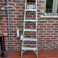 Front view of the metal step ladder leaning against brick wall with visible steps and top platform