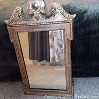 Full view of an ornate neoclassical style giltwood mirror with decorative carved frame and central medallion at the top.