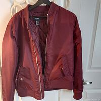 Front view of red men's bomber jacket with zipper open showing quilted lining, flap pockets with metal snap buttons, ribbed cuffs and waistband.