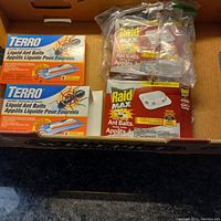 Top view showing 2 unopened Terro Liquid Ant Baits boxes and a partially used Raid Max Ant Baits box with bait station and sachets in plastic bag.