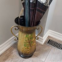 Metal umbrella holder with 4 umbrellas inside, showing decorative leaf design and two side handles.