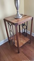 Side view of one wood end table showing wood finish and black metal decorative side panel with geometric design.