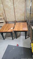 Two wooden end tables with natural wood tops and green painted legs shown from front and top angle in a basement with shelving and insulation in background.