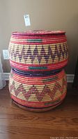 Two stacked handwoven decorative baskets with Middle Eastern geometric patterns in red, purple, yellow, and green colors.
