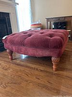 Side view showing tufted fabric upholstery and carved wooden legs of the ottoman.