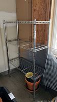 Full view of the stainless steel 4-shelf wire shelving unit in a garage space, showing the entire height and width of the unit with some pots on the bottom shelf.