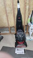 Front view of black Bissell ProHeat 2X Lift-Off Pet steam cleaner with detachable carpet cleaner and instruction manual on floor.
