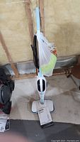 Full upright view of the DOKER steam cleaner with attached mop pad and power cord wrapped around handle.