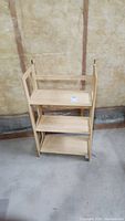 Fold flat wooden storage shelf standing upright showing three shelves and legs in a basement setting.