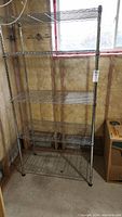 Front view of 5-shelf metal wire shelving unit with 5 evenly spaced shelves, standing against an unfinished basement wall.