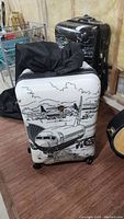 White Heys suitcase with black and white airplane and airport runway graphic design on the front, placed on wooden floor.